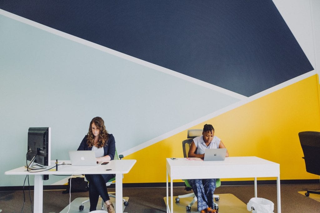 Two women working in an office on spaced out desks 